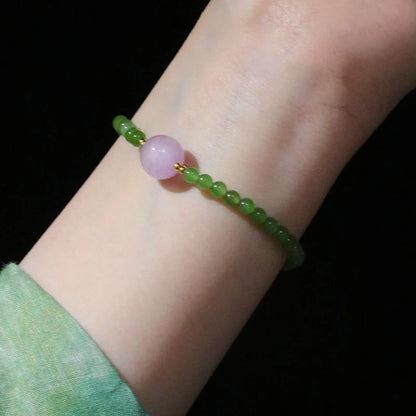 Womans hand wearing a pink crystal and green jade beaded bracelet in modern chinese style
