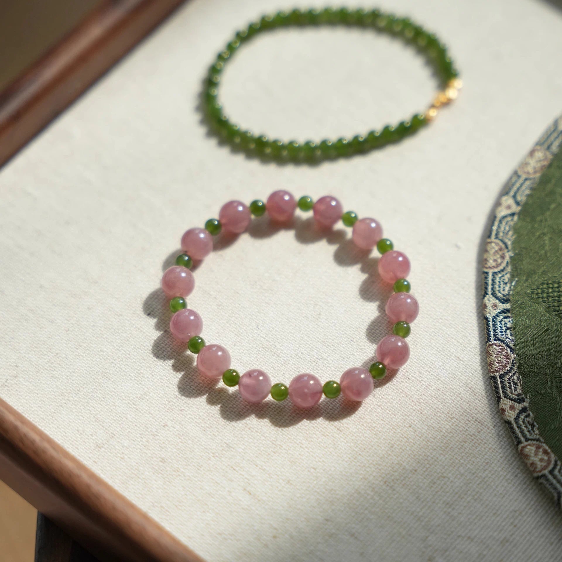 Womans hand wearing a pink crystal and green jade beaded bracelet in modern chinese style