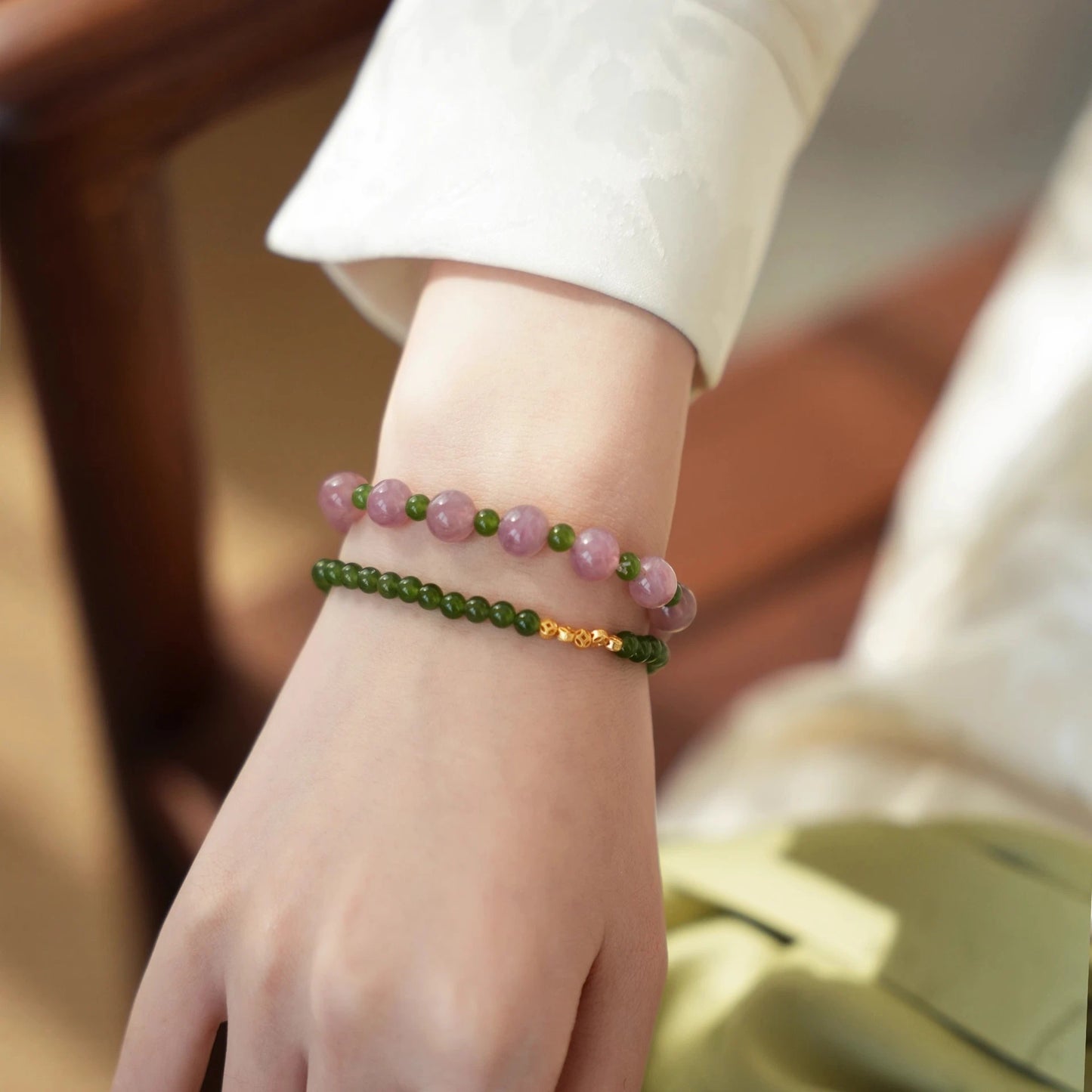 Womans hand wearing a pink crystal and green jade beaded bracelet in modern chinese style