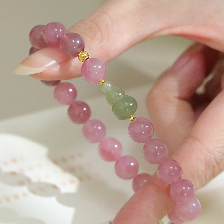 Womans hand wearing a pink crystal and green jade beaded bracelet in modern chinese style
